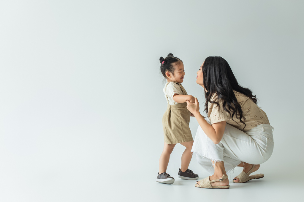 comprimento total de feliz asiático criança criança segurando as mãos com elegante mãe no cinza - Foto, Imagem