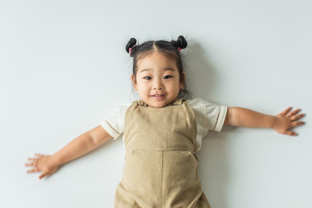 alto ângulo vista de feliz asiático criança menina com estendido mãos no cinza - Foto, Imagem