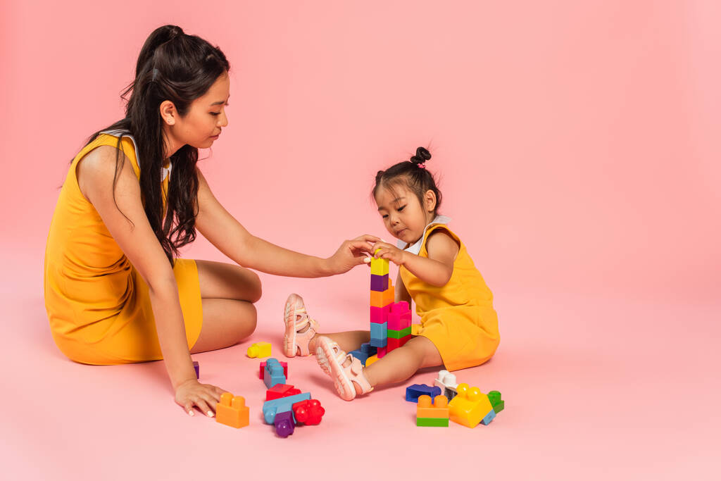 asian woman and daughter sitting and playing building blocks on pink  - Photo, Image