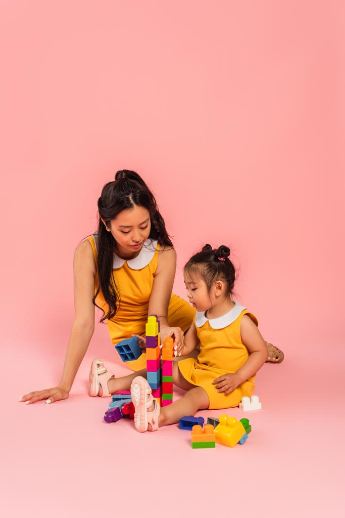 brunette aasialainen nainen ja tytär istuu ja pelaa rakennuspalikoita vaaleanpunainen  - Valokuva, kuva