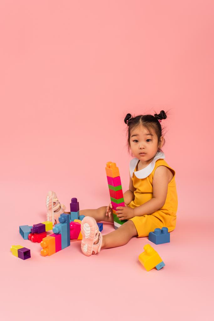 aziatische peuter kind in jurk spelen bouwstenen op roze  - Foto, afbeelding