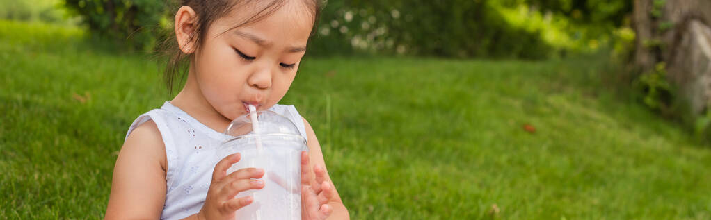 asian toddler kid in yellow dress drinking tasty milkshake through straw, banner - Photo, Image