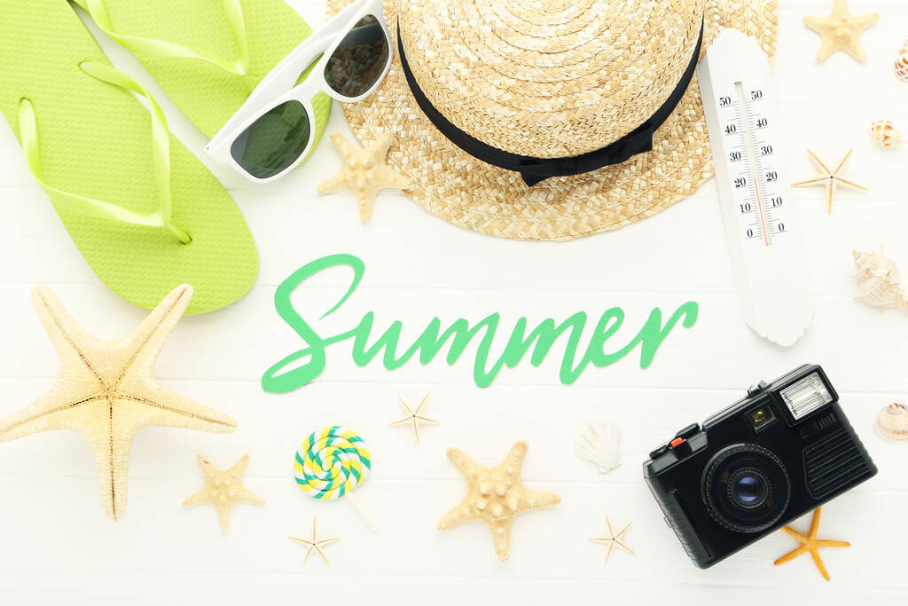 Κείμενο Καλοκαίρι με σαγιονάρες, ψάθινο καπέλο, κοχύλια, θερμόμετρο και κάμερα σε λευκό ξύλινο φόντο - Φωτογραφία, εικόνα