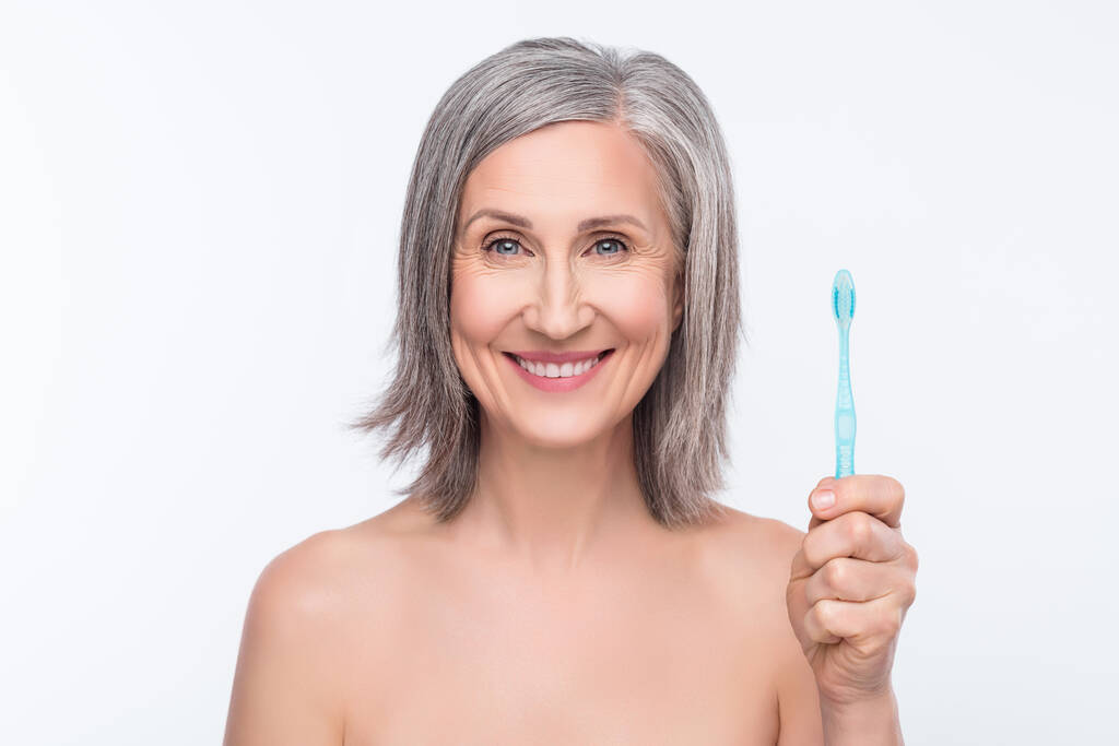 Фото щасливої красивої біловолосистої старої веселої жінки тримає руку зубна щітка посмішка гігієна ізольована на сірому кольоровому фоні
 - Фото, зображення