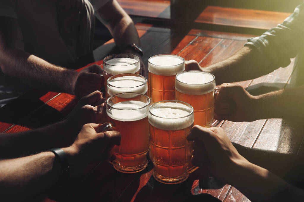 Друзья звонят в стаканы с пивом за столом, крупным планом - Фото, изображение