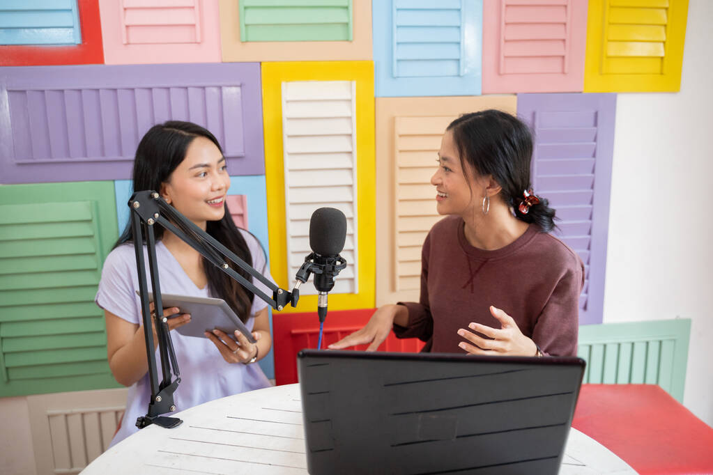 zwei Frauen unterhalten sich während eines Podcasts mit Mikrofon und Tablet - Foto, Bild