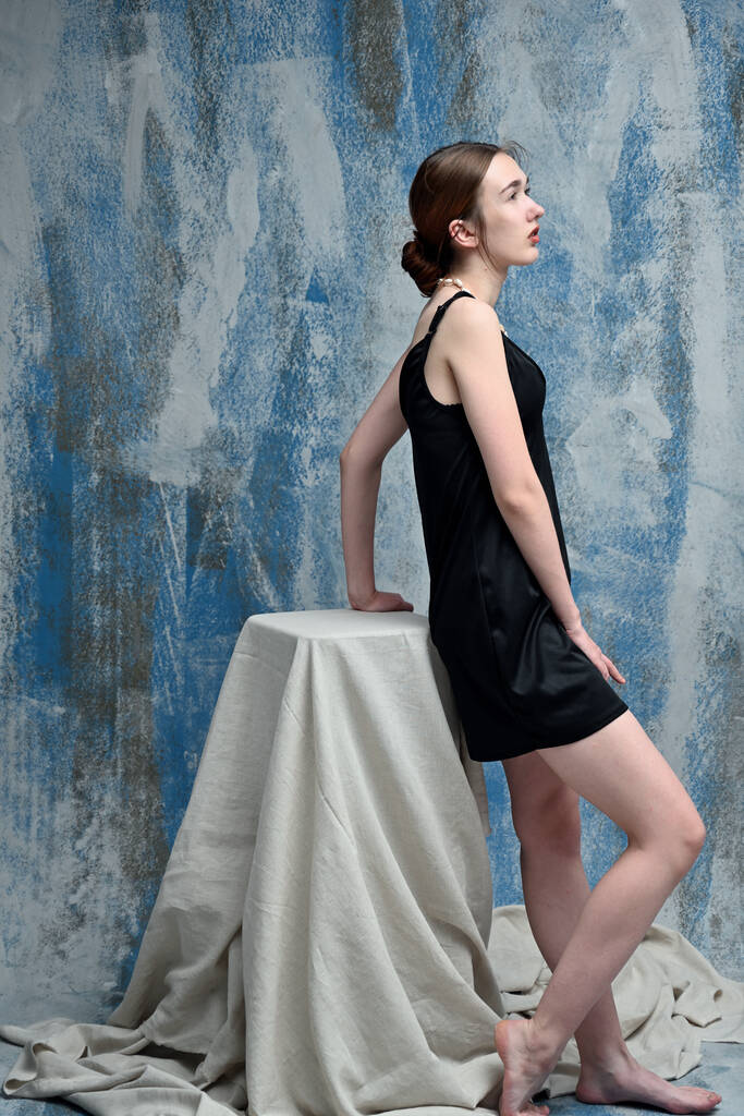Тонка модель в чорній сукні в студії, що стоїть на синьому фоні
 - Фото, зображення