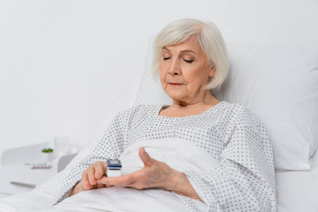 Starší žena používající digitální oximetr na rozmazaném popředí v nemocnici  - Fotografie, Obrázek