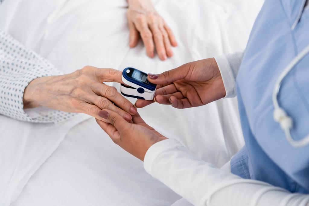 Vue recadrée de l'oxymètre de fixation de l'infirmière afro-américaine sur le doigt du patient âgé  - Photo, image