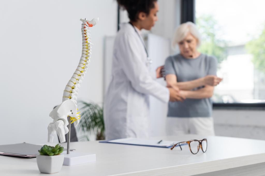 Modelo médico de coluna vertebral perto de médico inter-racial e paciente em fundo turvo  - Foto, Imagem