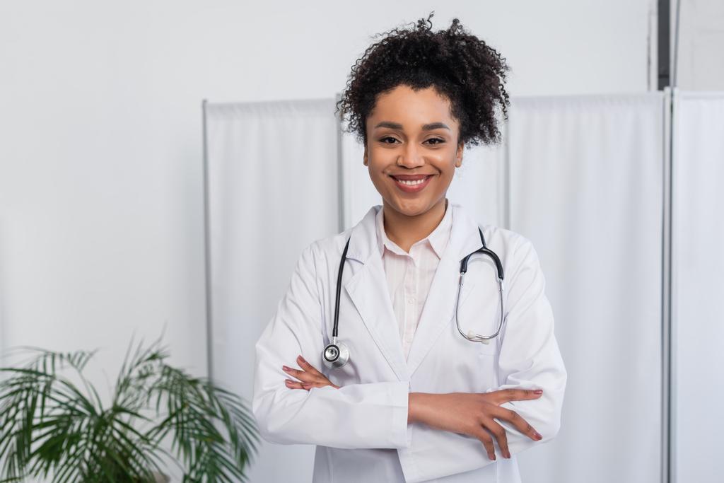 Hymyilevä afrikkalainen amerikkalainen lääkäri stetoskooppi seisoo ristissä kädet  - Valokuva, kuva