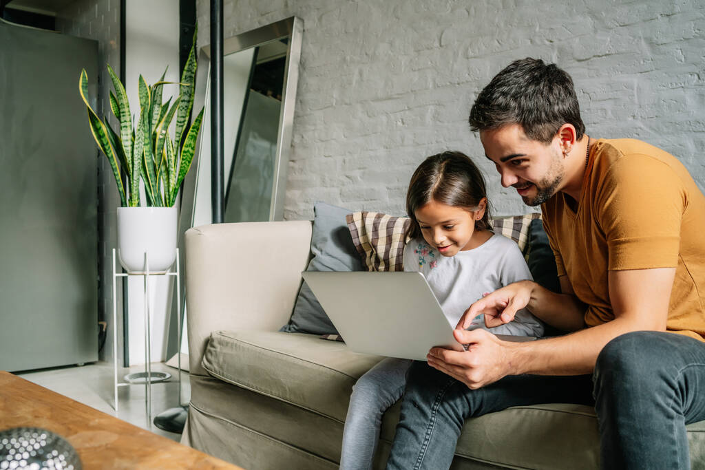 Маленькая девочка и ее отец используют ноутбук вместе дома. - Фото, изображение