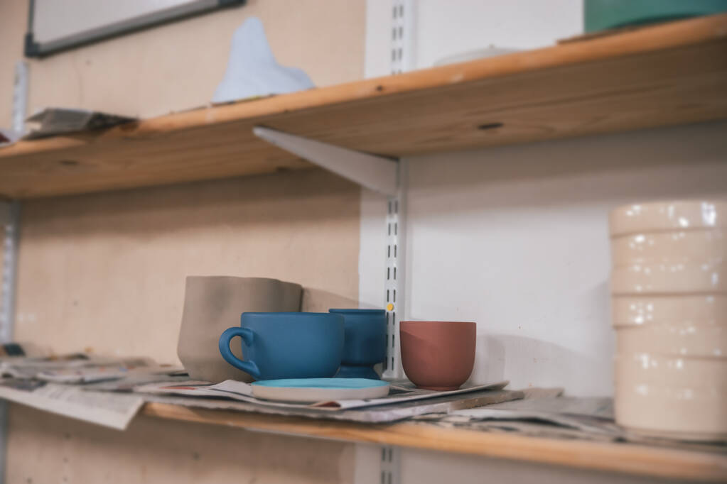 Um close-up de diferentes vasos de argila e copos nas prateleiras em uma oficina - Foto, Imagem