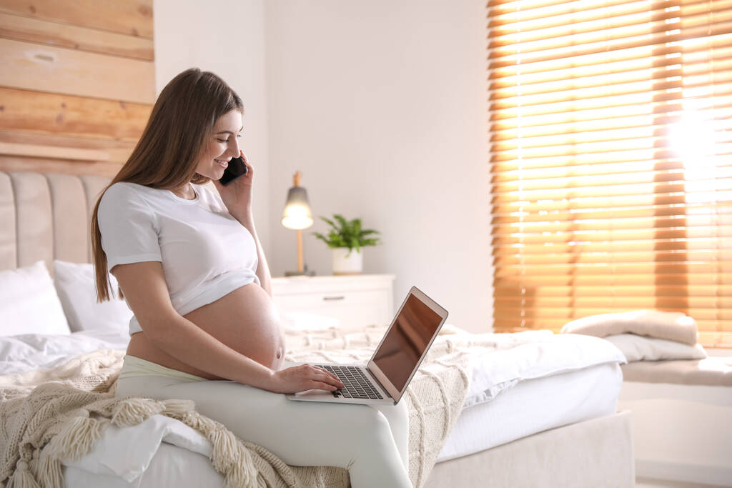 Беременная женщина, работающая дома на кровати, место для смс. Отпуск по беременности - Фото, изображение