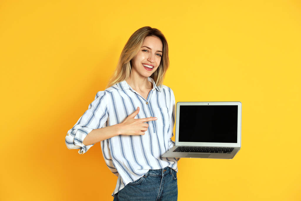 Jonge vrouw met moderne laptop op gele achtergrond - Foto, afbeelding