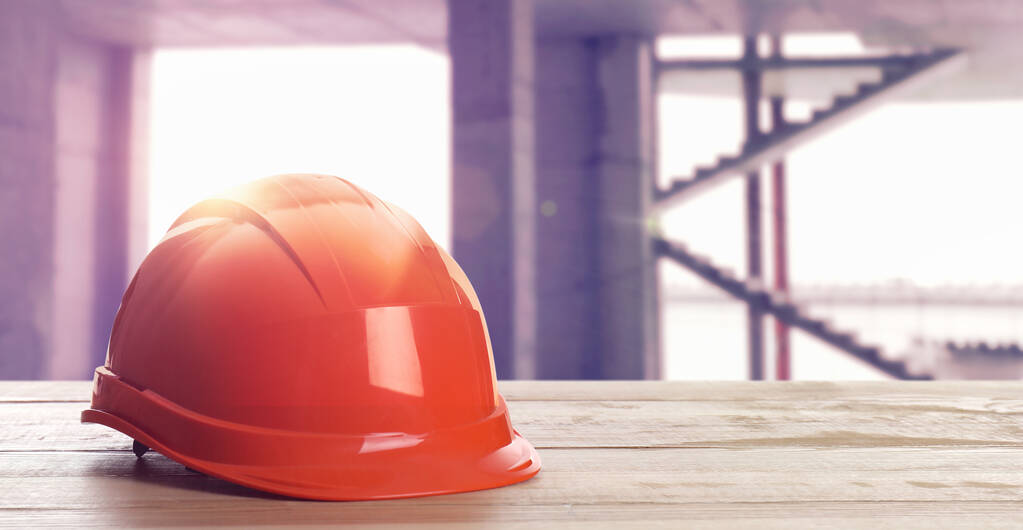 Hard hat on wooden surface at construction site with unfinished building. Space for text  - Photo, Image