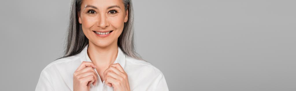 happy asian woman touching collar of white shirt isolated on grey, banner - Photo, Image