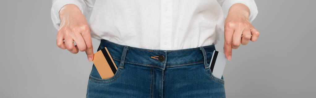 vista parcial de la mujer que toma tarjetas de crédito de bolsillos de jeans aislados en gris, bandera - Foto, Imagen