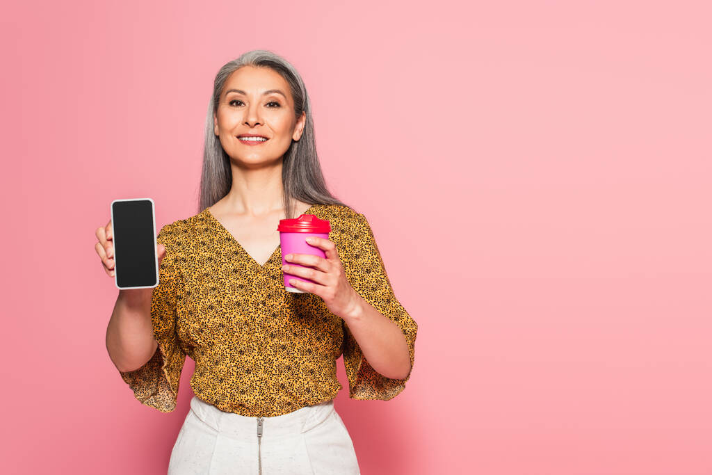 hymyilevä aasialainen nainen kahvia mennä näyttämään älypuhelin tyhjä näyttö vaaleanpunainen  - Valokuva, kuva