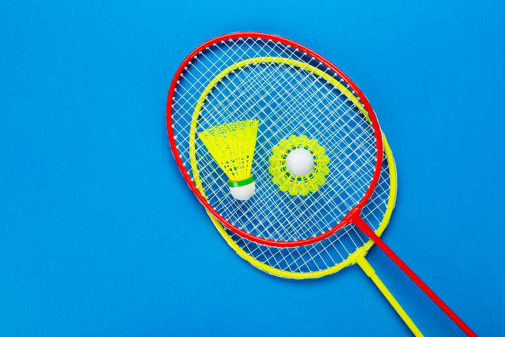 Twee shuttlecock en badminton rackets op blauwe achtergrond. Actief recreatie- en sportconcept. Ruimte voor tekst. Bovenaanzicht. - Foto, afbeelding