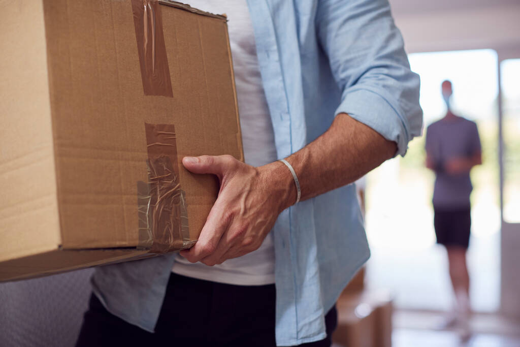 Közelkép a férfi pár cipeli dobozok a bejárati ajtón keresztül az új otthon a költözés napján - Fotó, kép