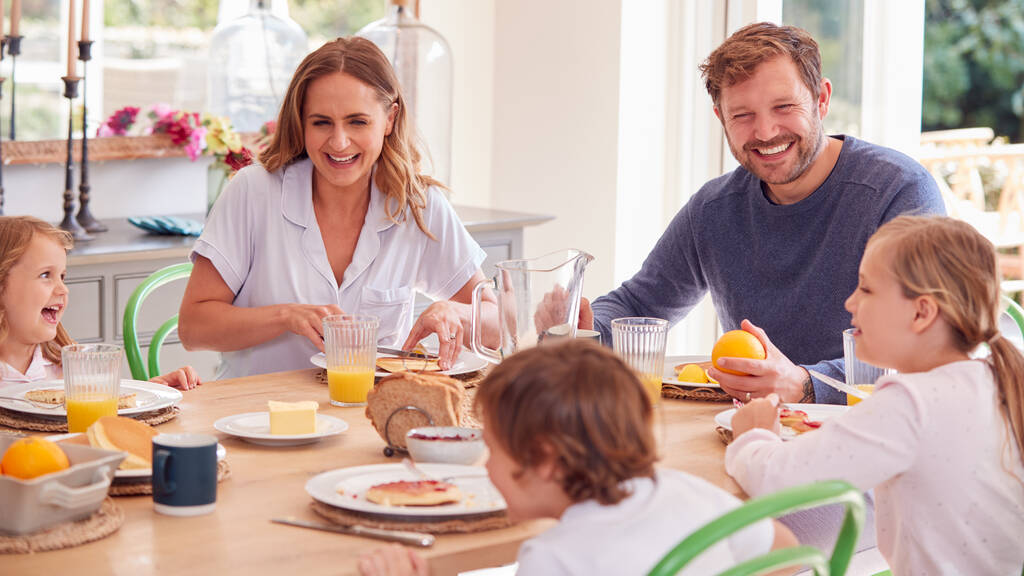 Сім'я носить піжаму сидячи навколо столу насолоджуючись сніданком з млинцями
 - Фото, зображення