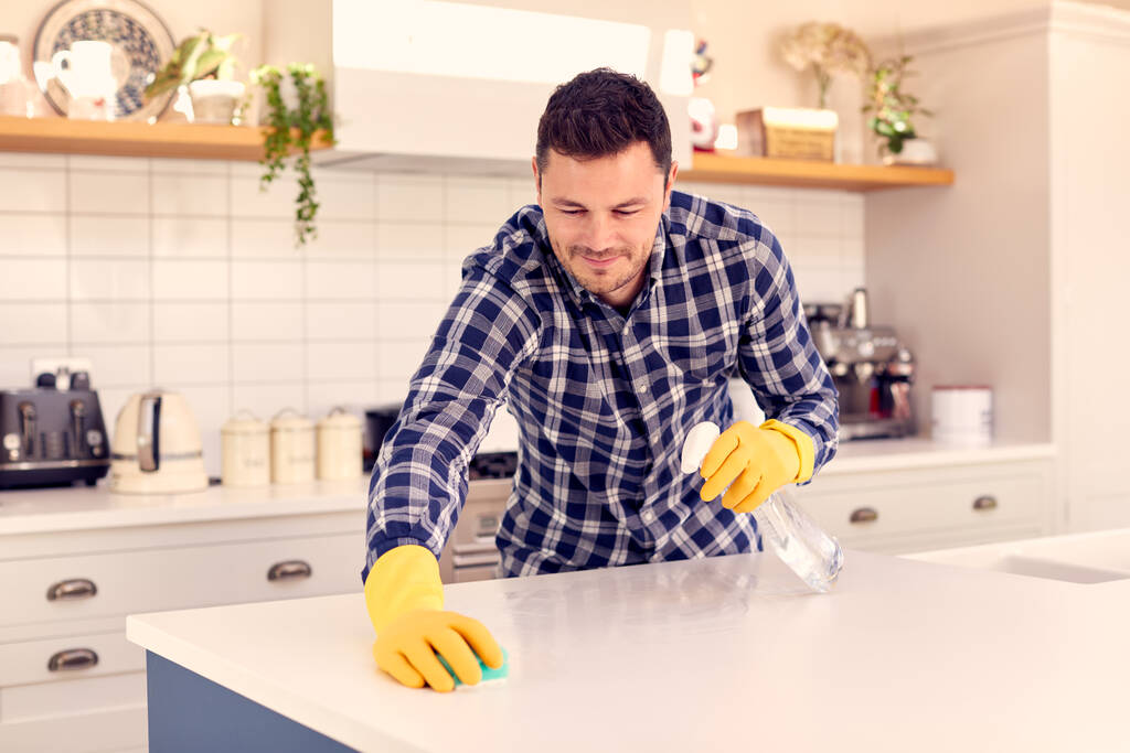 Mann zu Hause in Küche Hausarbeit erledigen und Arbeitsplatte mit Spray reinigen - Foto, Bild
