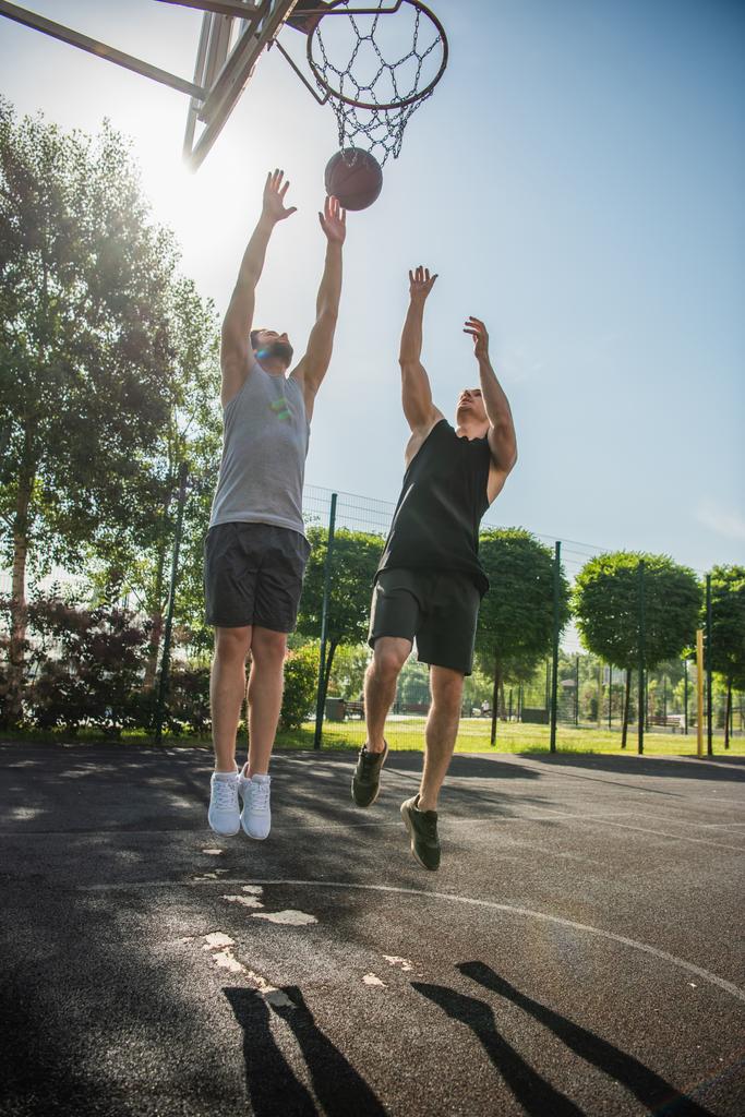 Jonge mannen springen in de buurt van bal en basketbal hoepel buiten  - Foto, afbeelding