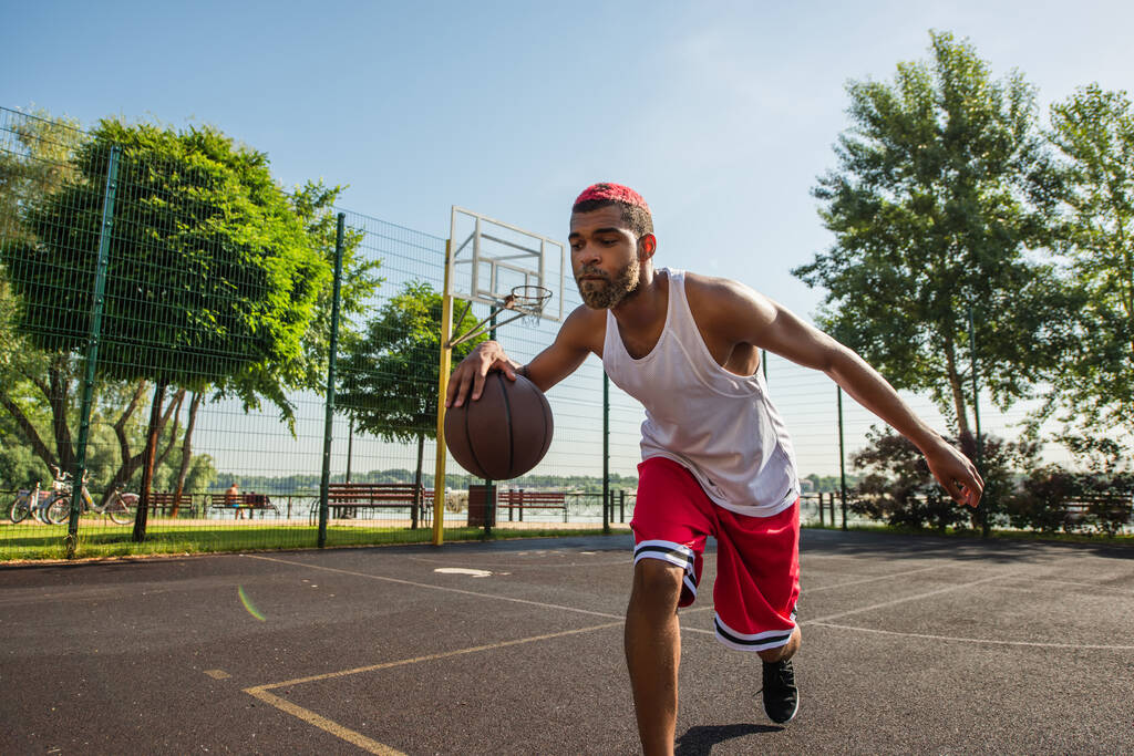 アフリカ系アメリカ人スポーツマンが野外遊び場でバスケットボールをする  - 写真・画像