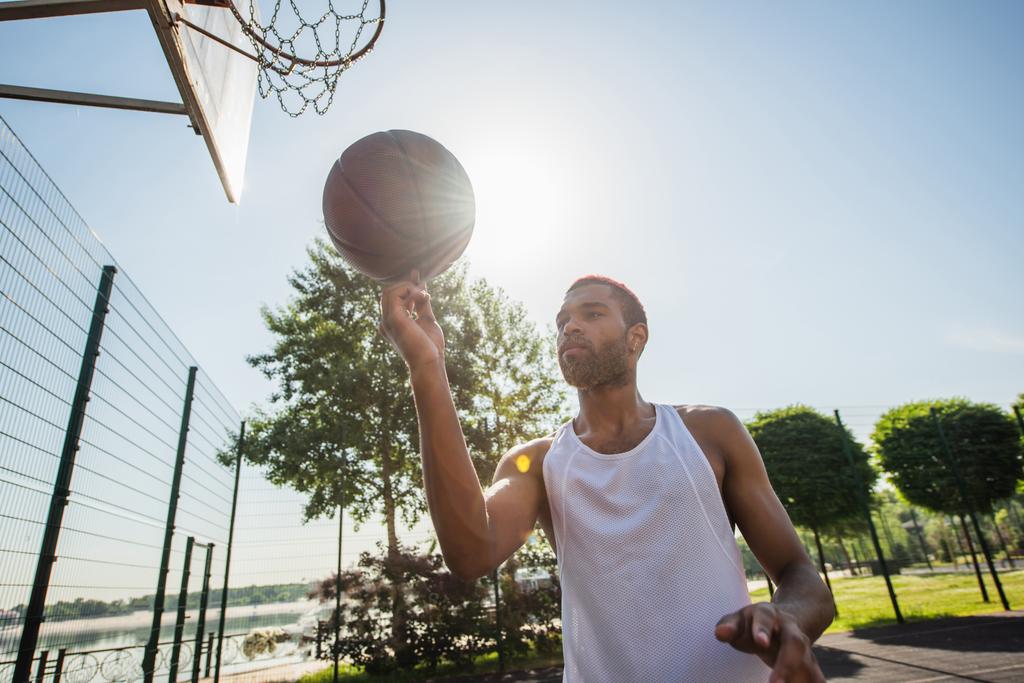 Junger afrikanisch-amerikanischer Mann hält tagsüber Basketballball im Freien  - Foto, Bild