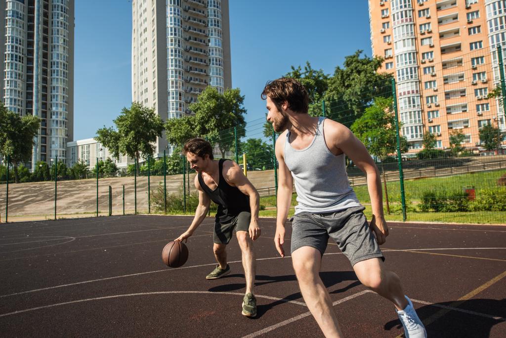 Vista lateral do homem correndo perto de amigo com bola de basquete no playground  - Foto, Imagem