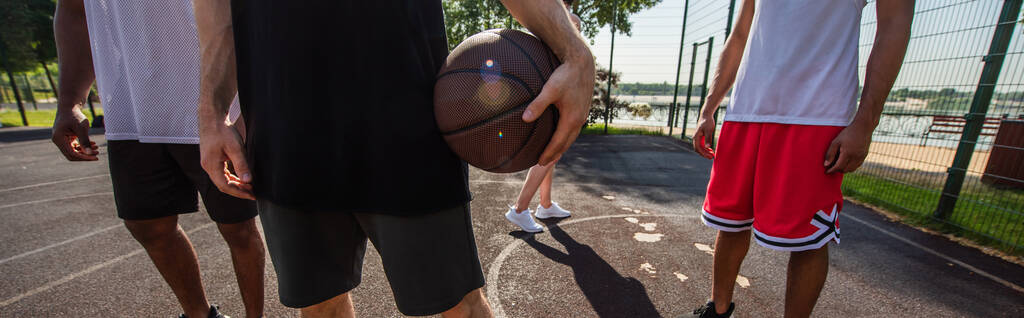 Vue recadrée du sportif avec ballon de basket debout près d'amis interracial, bannière  - Photo, image
