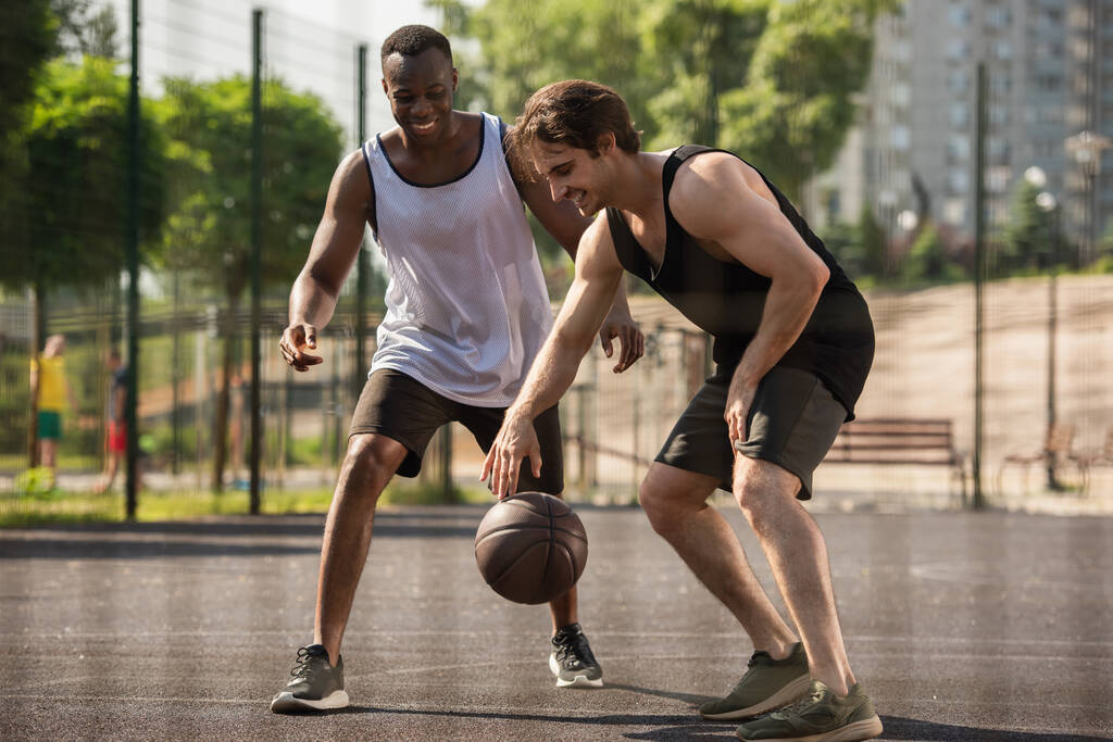 Uśmiechnięty międzyrasowy mężczyźni gra w koszykówkę na zewnątrz  - Zdjęcie, obraz