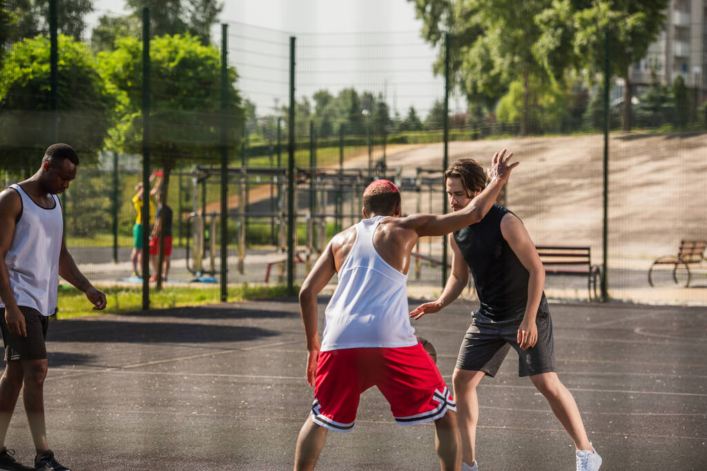 man spelen basketbal met afrikaanse amerikaanse vrienden op outdoor speeltuin  - Foto, afbeelding