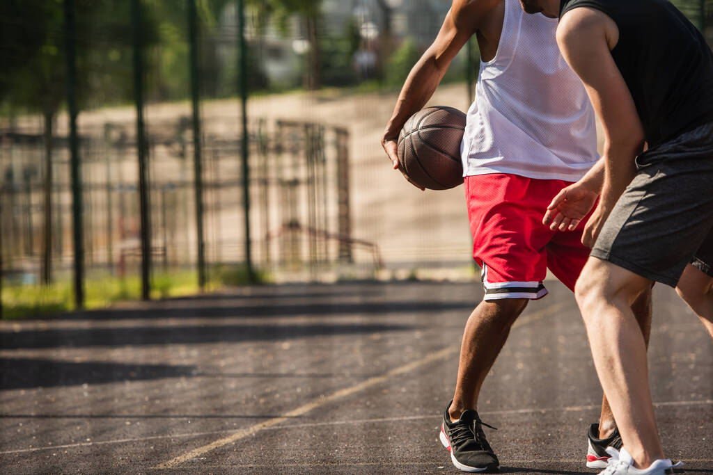 屋外で友人の近くにバスケットボールボールを保持アフリカ系アメリカ人スポーツマンの作物ビュー  - 写真・画像