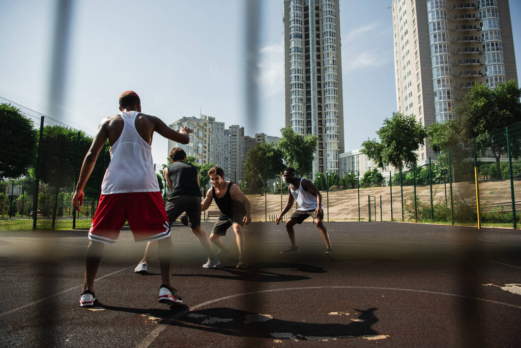 Młodzi wielonarodowi mężczyźni grający w koszykówkę na placu zabaw na ulicy miejskiej  - Zdjęcie, obraz