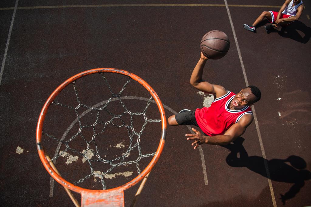 興奮したアフリカ系アメリカ人男性のトップビューとともにバスケットボールボールジャンプ近くフープ  - 写真・画像