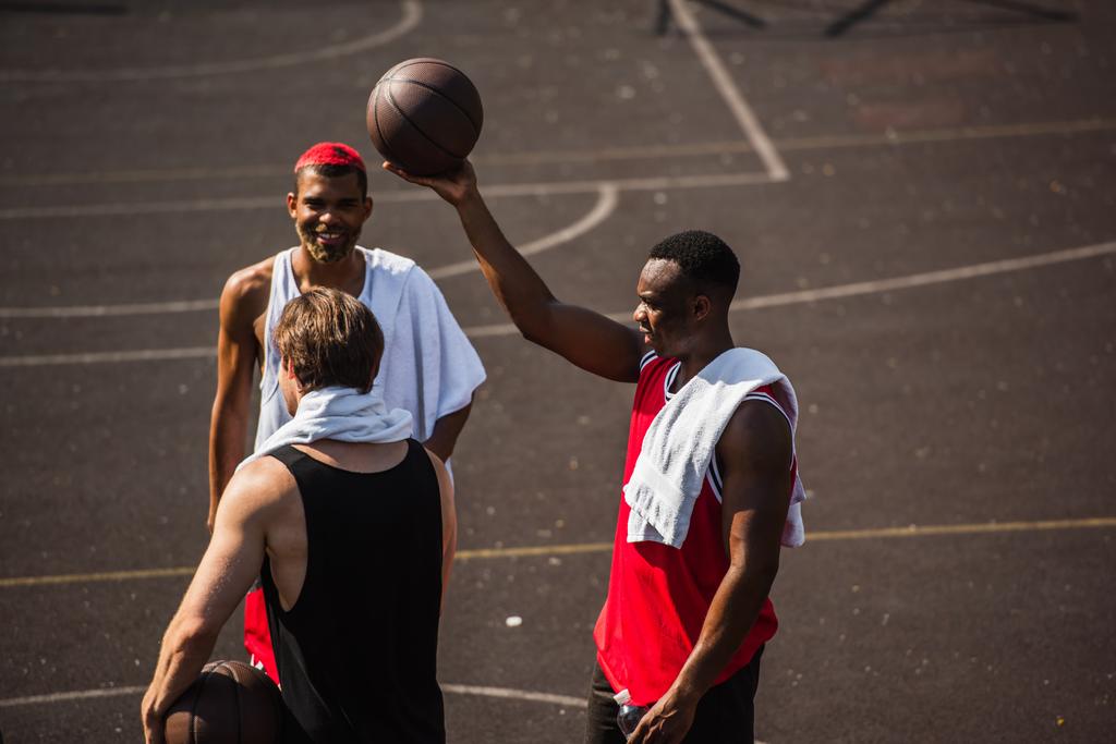 Межрасовые спортсмены с полотенцами и баскетбольными мячами на открытом воздухе  - Фото, изображение