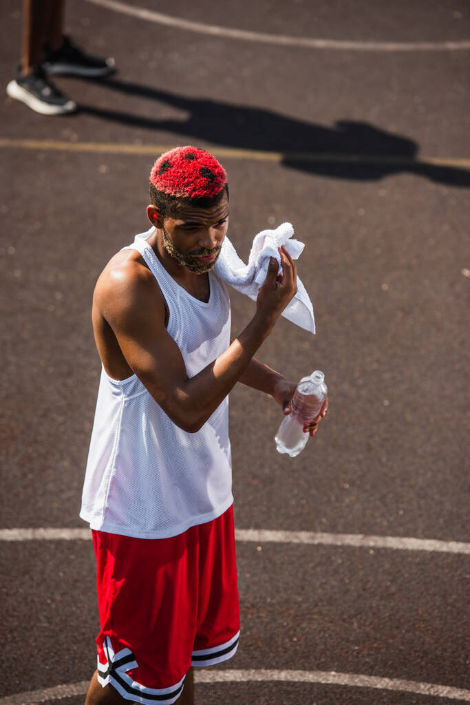 Hoge hoek uitzicht op de Afrikaanse Amerikaanse sportman met handdoek en fles water op de speelplaats  - Foto, afbeelding