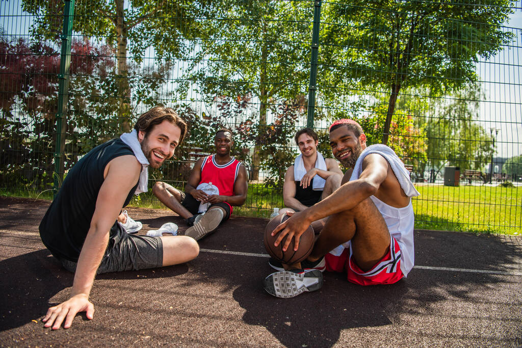 Gelukkige multi-etnische sporters op zoek naar camera op basketbal speeltuin  - Foto, afbeelding