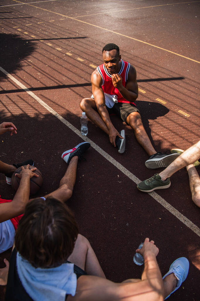 Blick von oben auf afrikanisch-amerikanischen Sportler im Gespräch mit Freunden mit Basketballball auf Spielplatz  - Foto, Bild