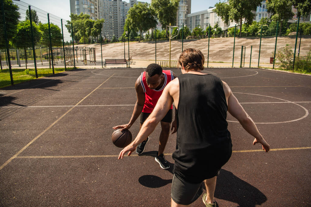 Monietniset miehet pelaavat koripalloa ulkona leikkikentällä päivällä  - Valokuva, kuva