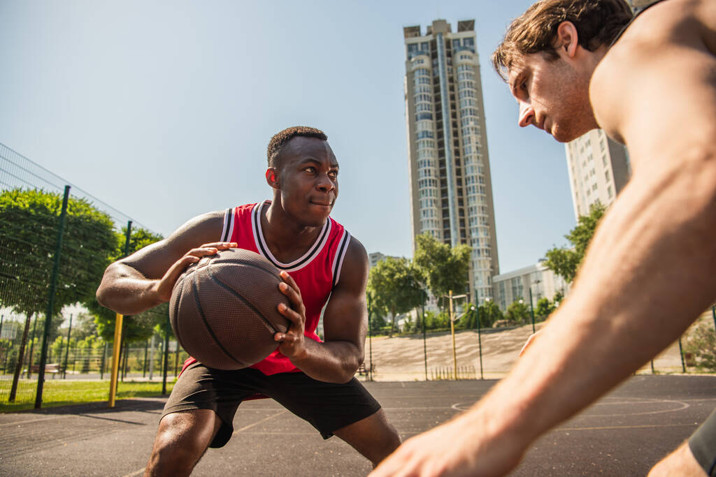 Jogador americano africano concentrado segurando bola de basquete perto de amigo durante a competição  - Foto, Imagem