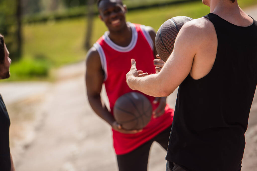 Sportowiec trzyma piłkę do koszykówki w pobliżu zamazanych przyjaciół na świeżym powietrzu  - Zdjęcie, obraz