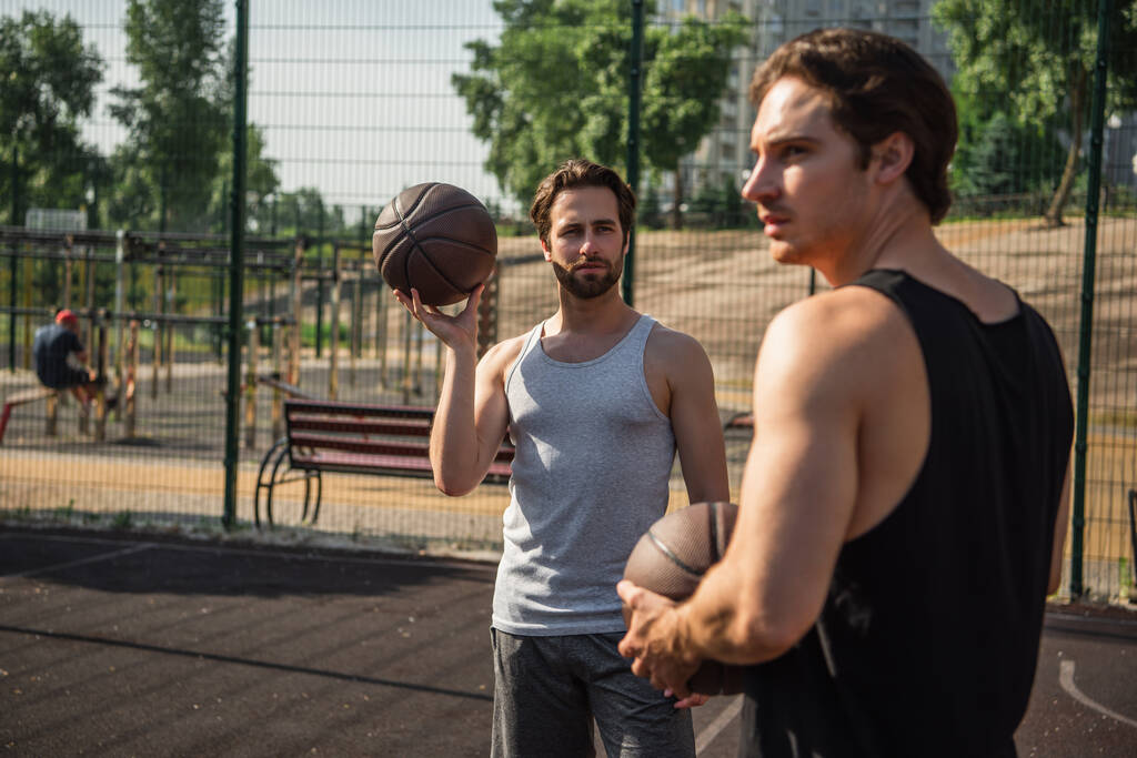 Mężczyzna trzyma piłkę do koszykówki w pobliżu zamazanego przyjaciela na placu zabaw  - Zdjęcie, obraz