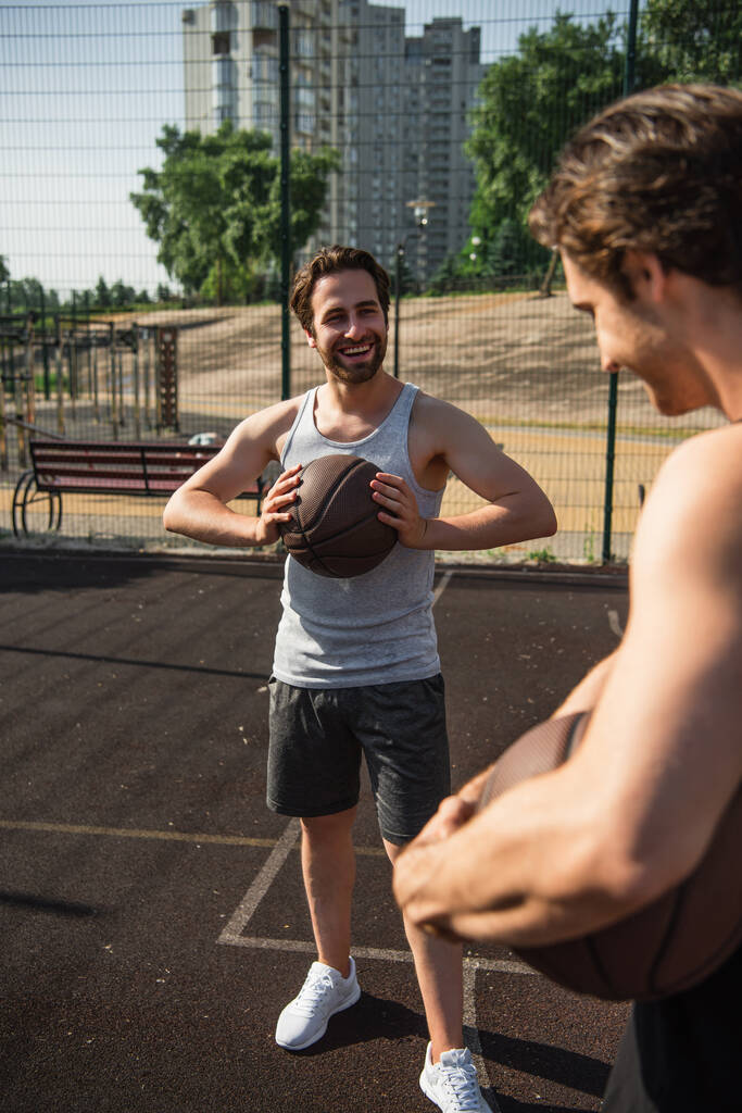 Gülen adam basketbol topunu sahada bulanık arkadaşının yanında tutuyor.  - Fotoğraf, Görsel