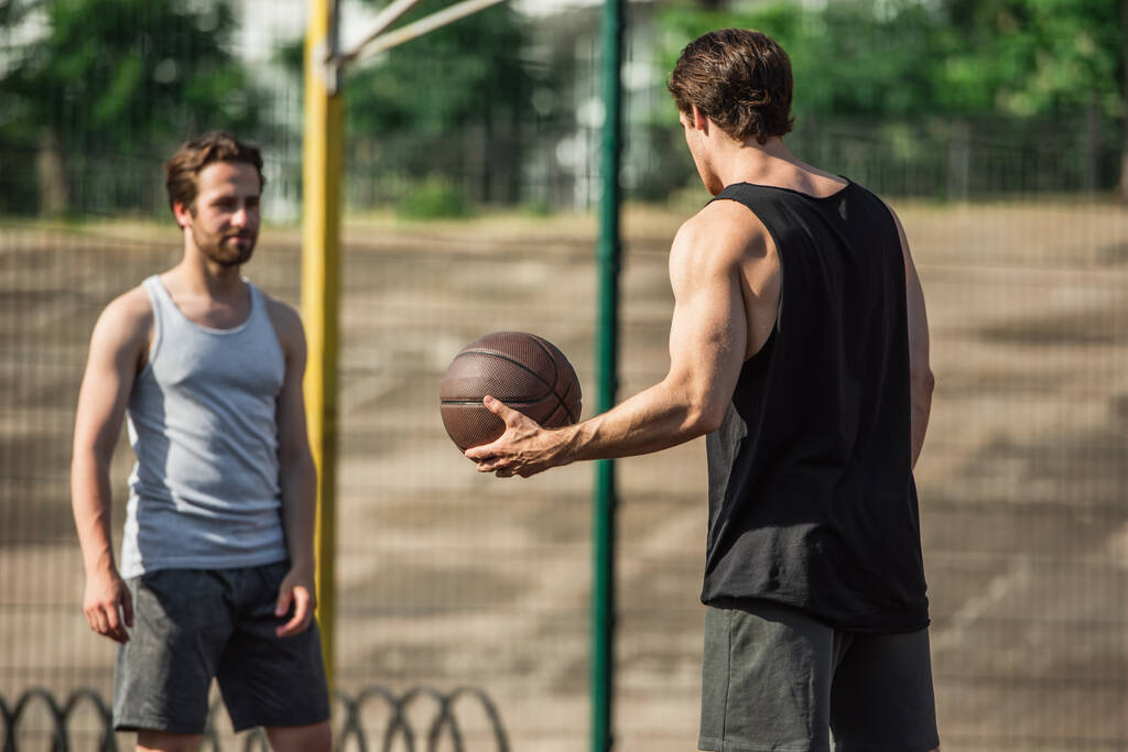 Atlétikai férfi kezében kosárlabda közelében elmosódott barát szabadban  - Fotó, kép