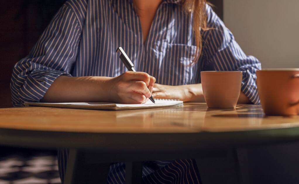 ペンでノートを取り、女性の手は、コーヒーハウスでコーヒーカップと木製のテーブルの上に日記に計画を書く。女とともに木製デスクでプランナーとお茶マグカップ閉じ - 写真・画像