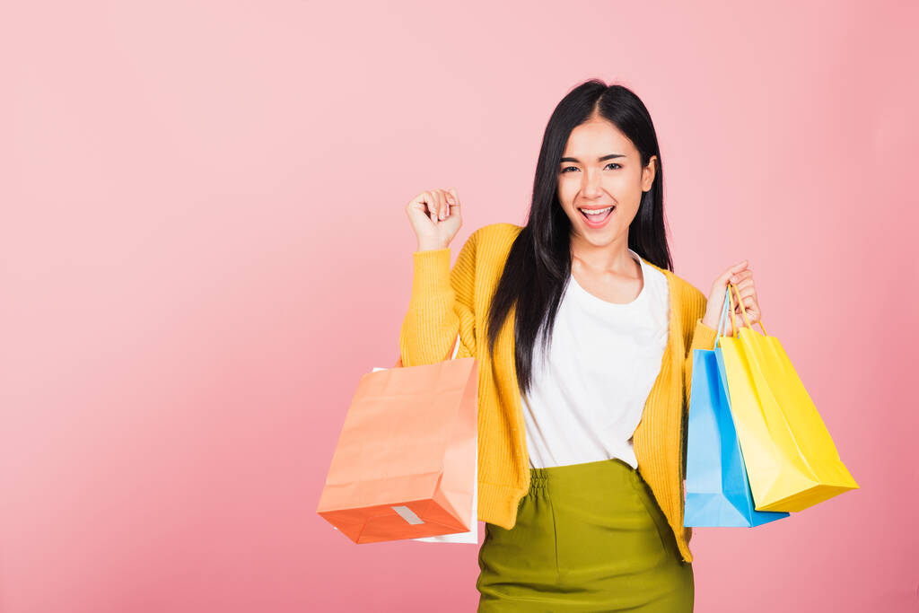 Portrait d'Asiatique heureux belle jeune femme adolescent shopper souriant debout excité tenant sacs à provisions en ligne multicolore coloré en été, prise de vue en studio isolé sur fond rose avec espace de copie - Photo, image