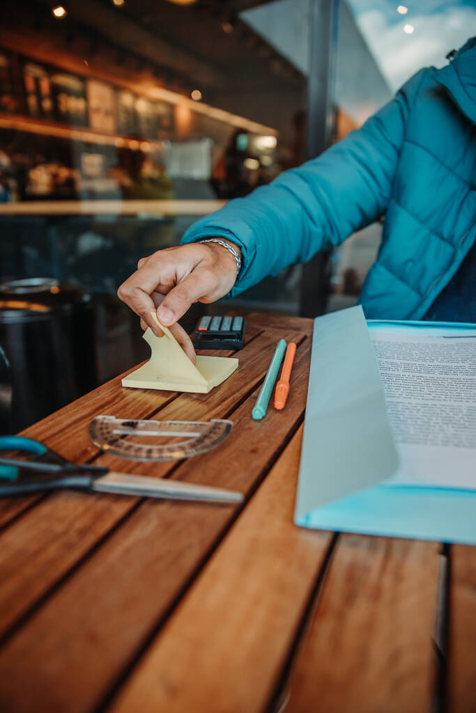 Egy közeli kép egy diákról, aki ragacsos sárga hangot vesz fel, miközben egy kávézóban tanul. - Fotó, kép
